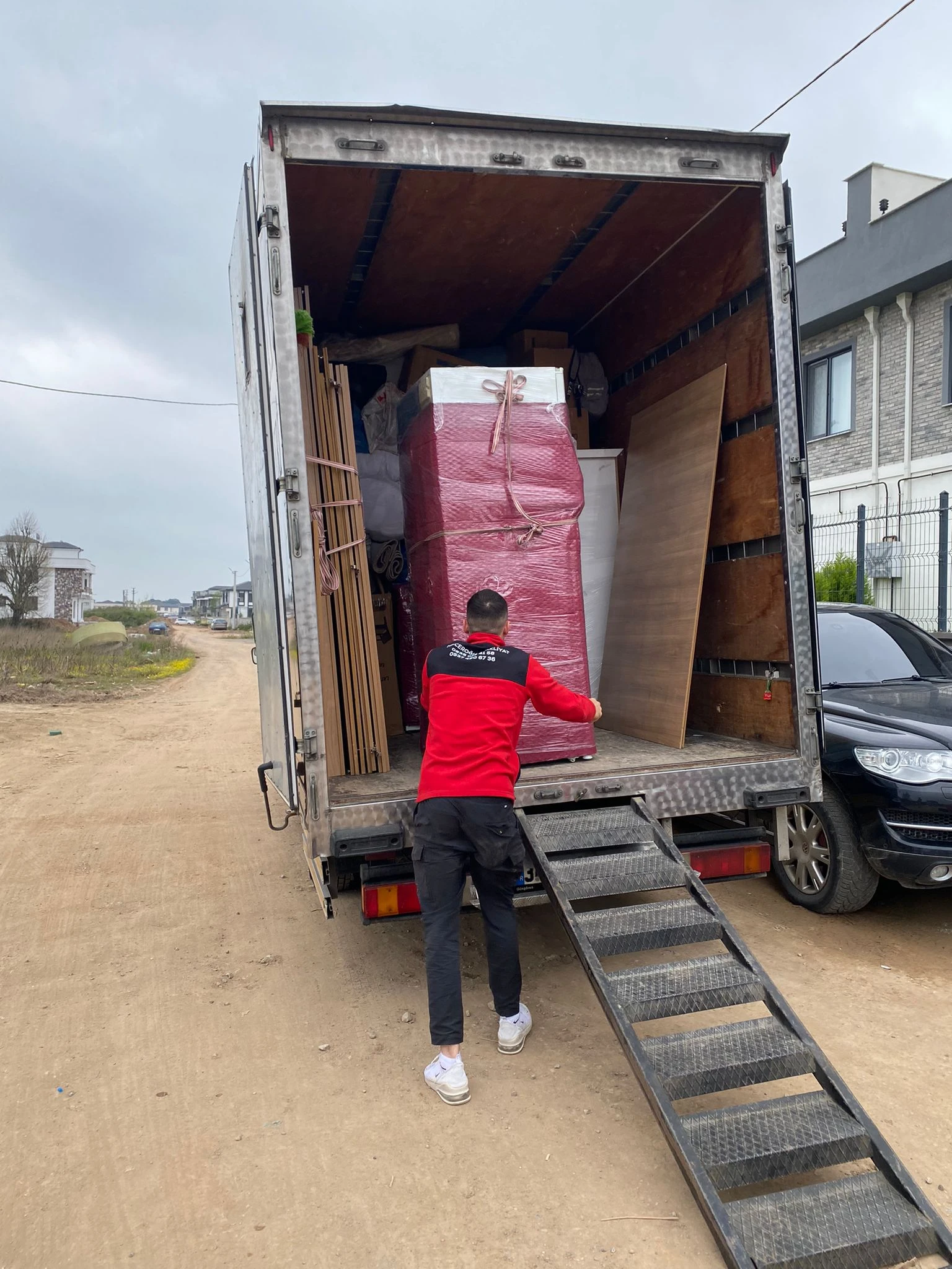 A mover in a blue t-shirt carrying a large item wrapped in yellow cling film.
